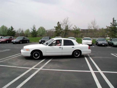 1998 Ford Crown Victoria - A white 1998 Ford Crown Victoria is parked in a lot with several other vehicles visible.