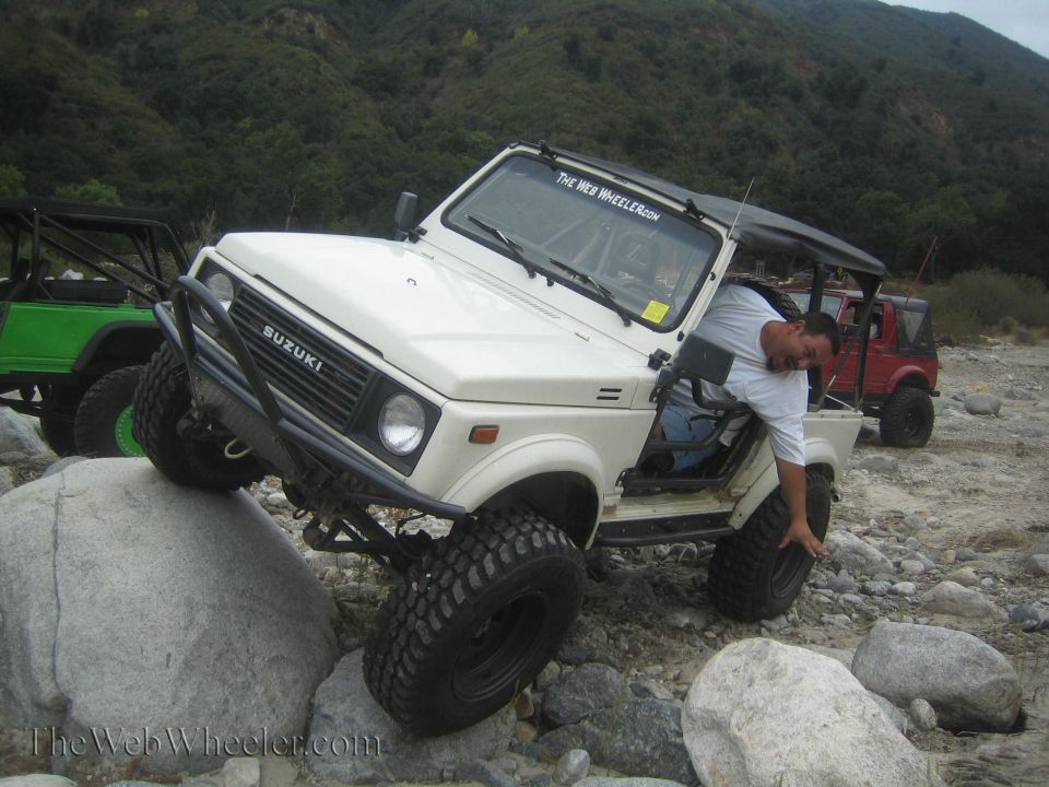White 1987 Suzuki Samurai on rocks, driver leaning out