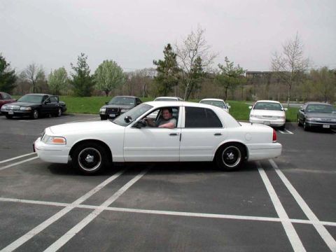 1998 Ford Crown Victoria - Side view of a white 1998 Ford Crown Victoria with a driver inside, parked in a lot.