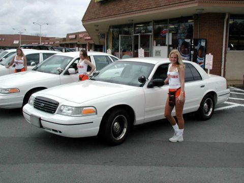1998 Ford Crown Victoria - Two white Ford Crown Victorias are parked in front of a building with two women standing next to them.