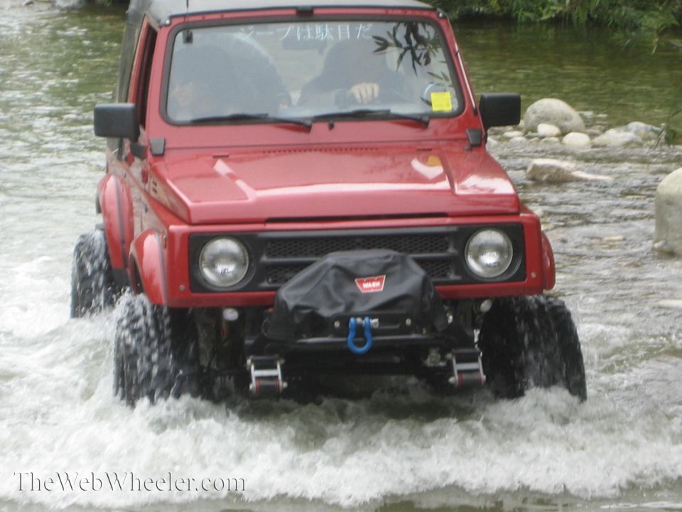 Red 1987 Suzuki Samurai driving through shallow water