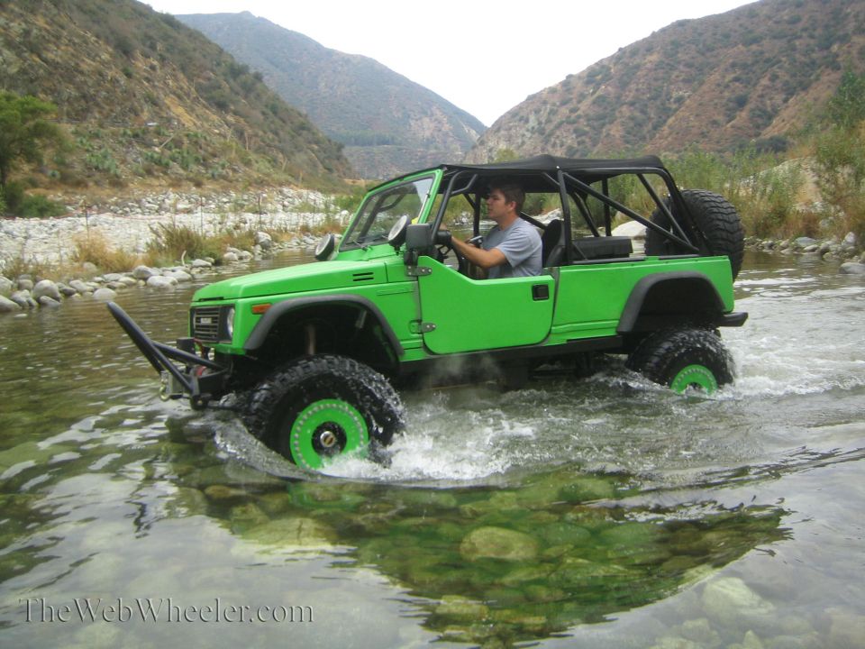 1987 Suzuki Samurai driving through a river, modified with large tires and a front bumper