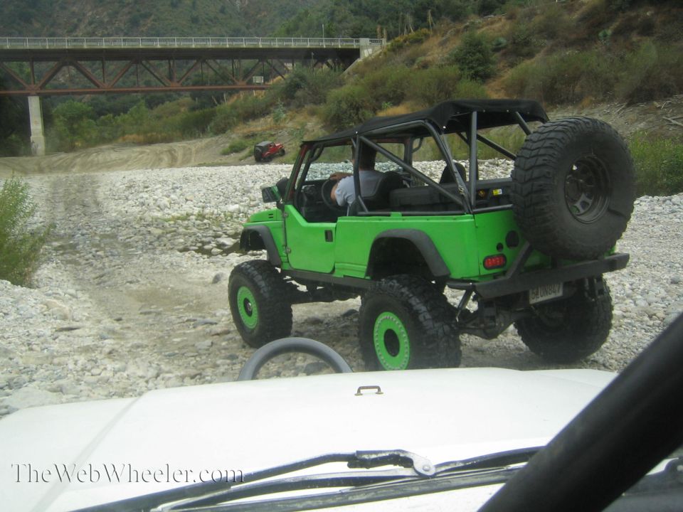 Green off-road vehicle with a roll cage and large tires, seen from behind and to the side