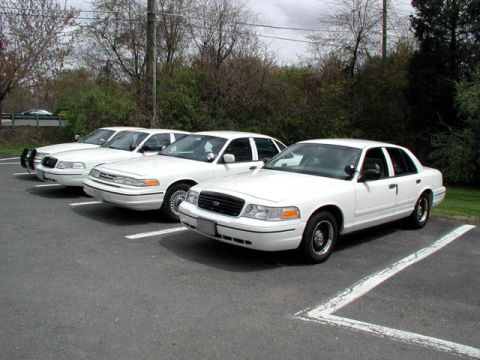 1998 Ford Crown Victoria - Four white Ford Crown Victoria police cars are parked in a lot, showing their front 3/4 views.