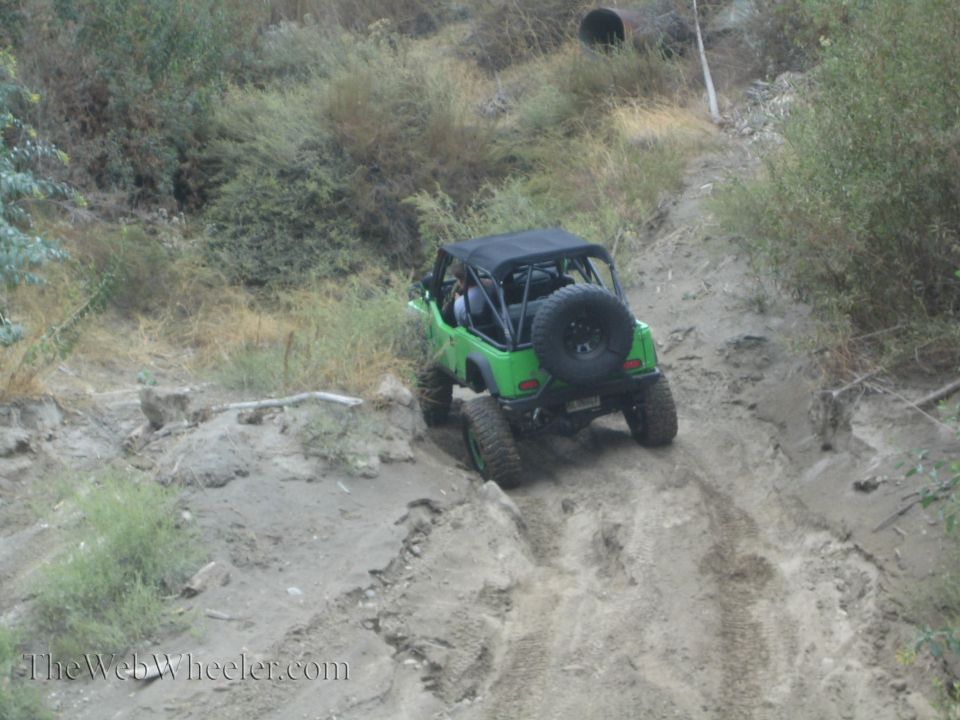 Green off-road vehicle with black soft top driving up a dirt hill