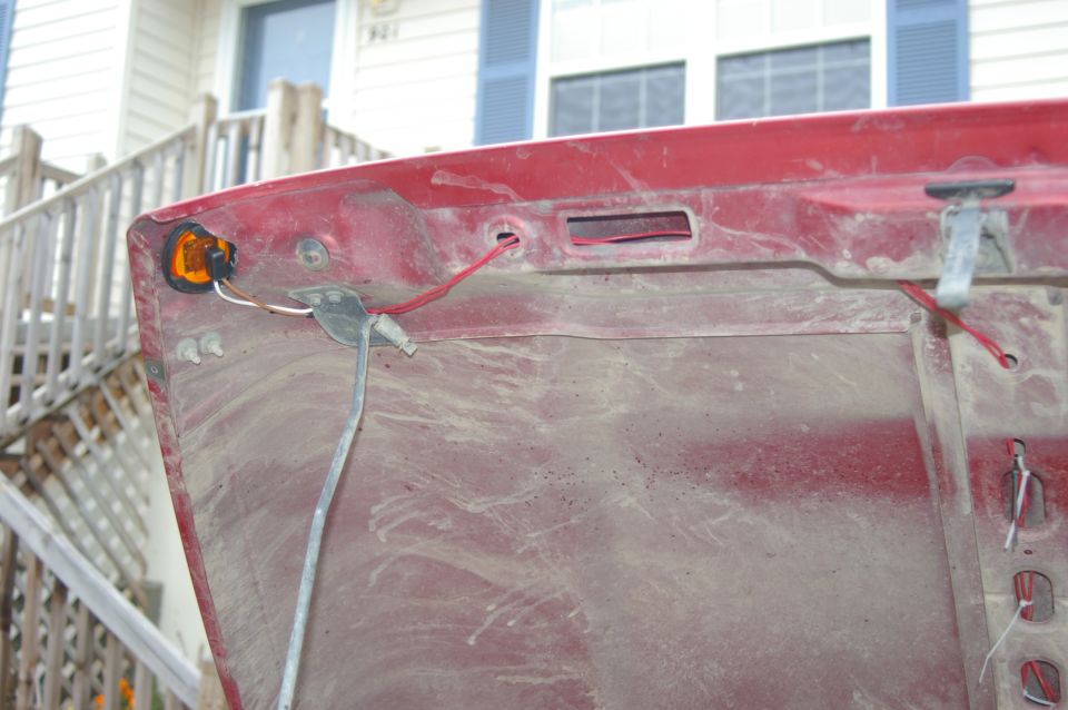 Underside of red car hood showing wiring and amber marker light assembly