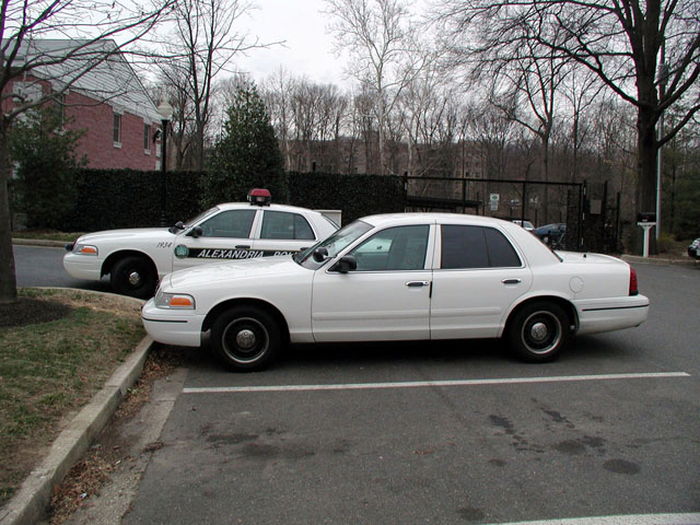 White Ford Crown Victoria sedan beside an Alexandria Police cruiser, side view