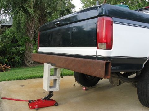1974 Ford F-100 - The rear bumper of a two-tone pickup truck is temporarily supported by a jack and cinder blocks.