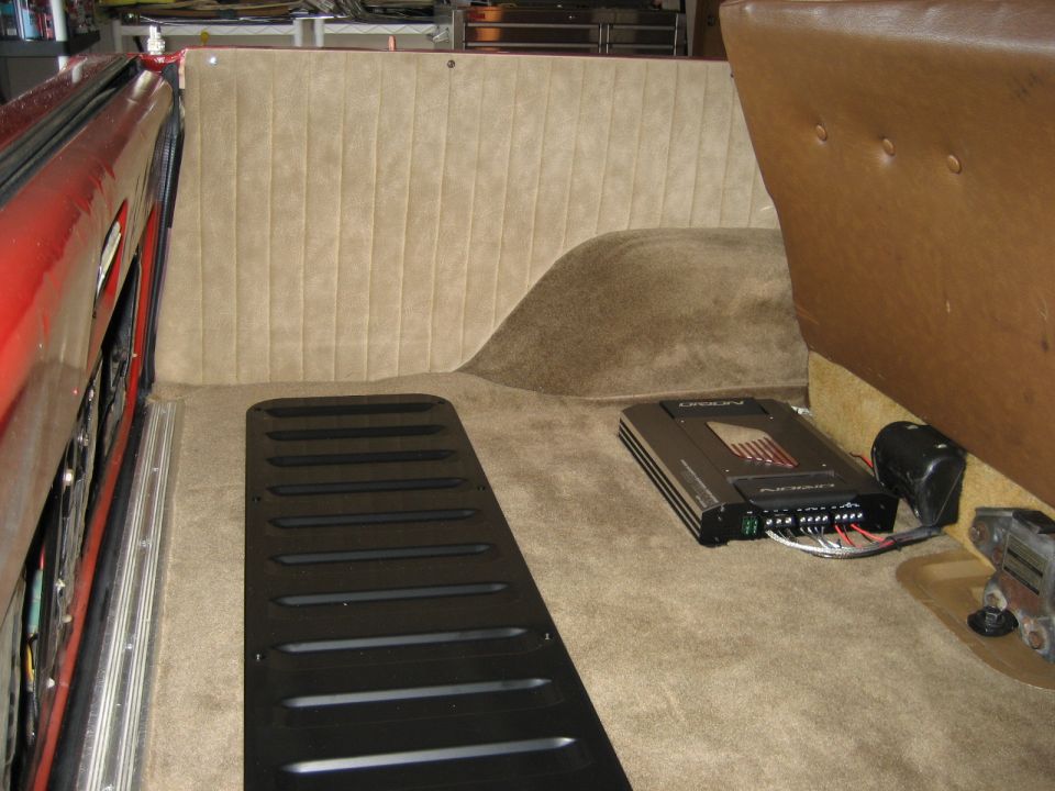 Car interior showing carpeted side panel, black floor mat, and audio amplifier