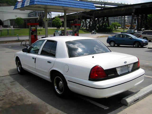 White Ford Crown Victoria sedan rear 3/4 view at a gas station.