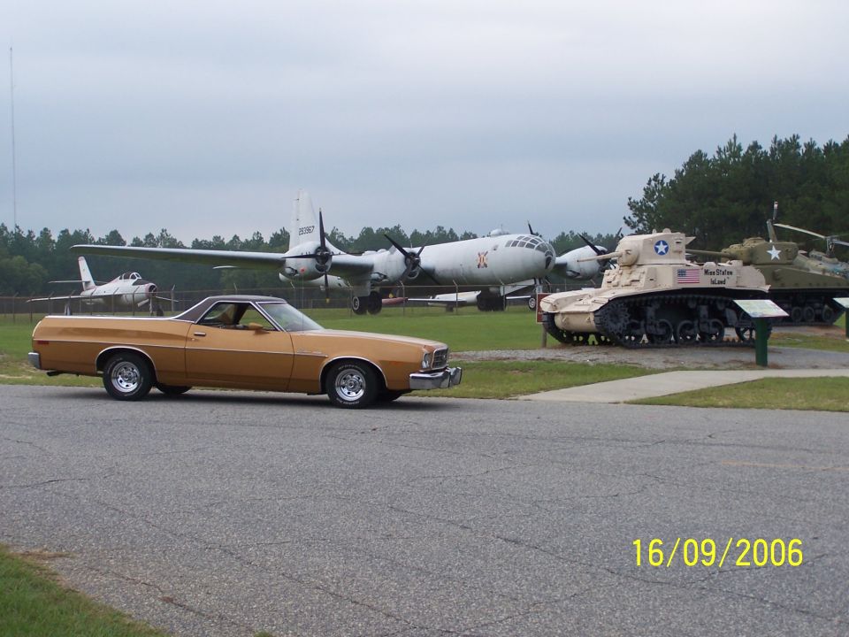 Gold Ford Ranchero in side view at a military museum with bomber and tanks