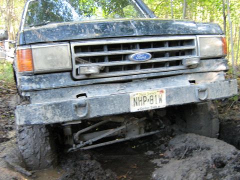 1990 Ford Bronco - A black Ford truck is stuck in mud, showing its front grille and license plate.