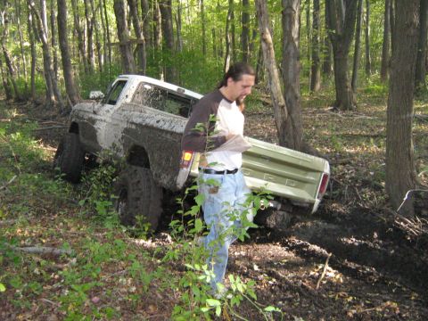 1990 Ford Bronco - A man stands near a mud-covered 1979 Ford F-Series pickup truck that appears to be stuck in a wooded area.