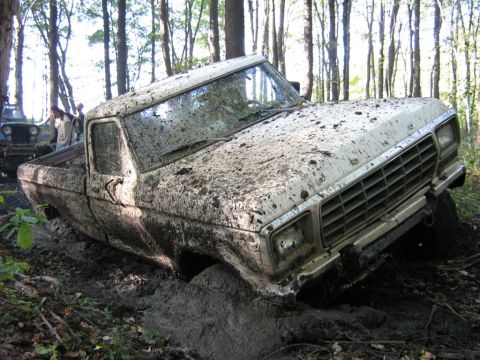 1990 Ford Bronco - Pickup truck stuck deep in mud off-road, with another vehicle nearby.