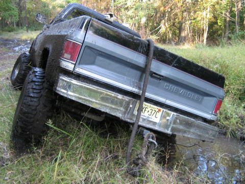 1990 Ford Bronco - A Chevrolet pickup truck is stuck in a muddy ditch, with its rear end partially submerged.