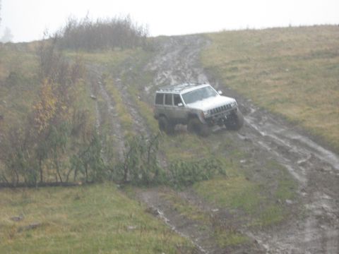 1995 Ford Bronco - A Jeep Cherokee XJ navigates a challenging muddy trail on a hill.