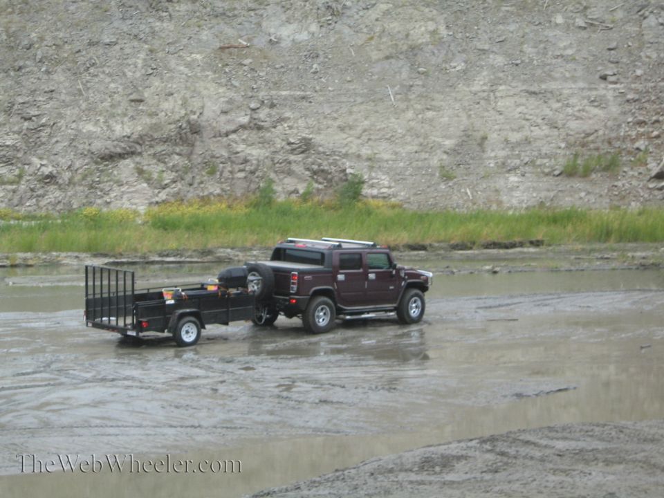 Dark red Hummer H2 SUV towing a black utility trailer through muddy water