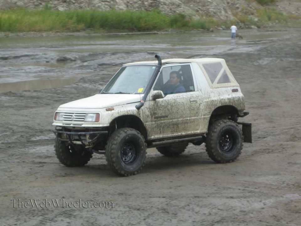 1987 Suzuki Samurai with snorkel and off-road tires driving in mud