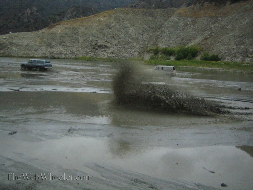 Two SUVs driving through a muddy area with one kicking up a large spray of mud