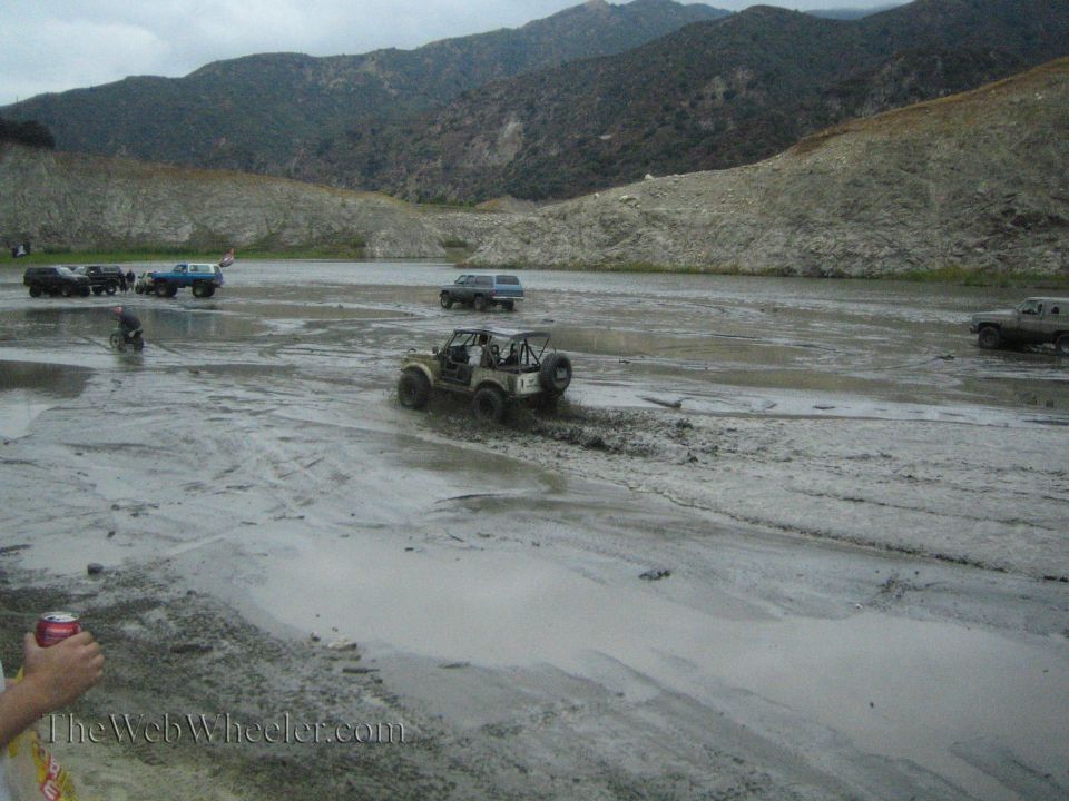 Off-road vehicles navigating a muddy terrain with mountains in the background