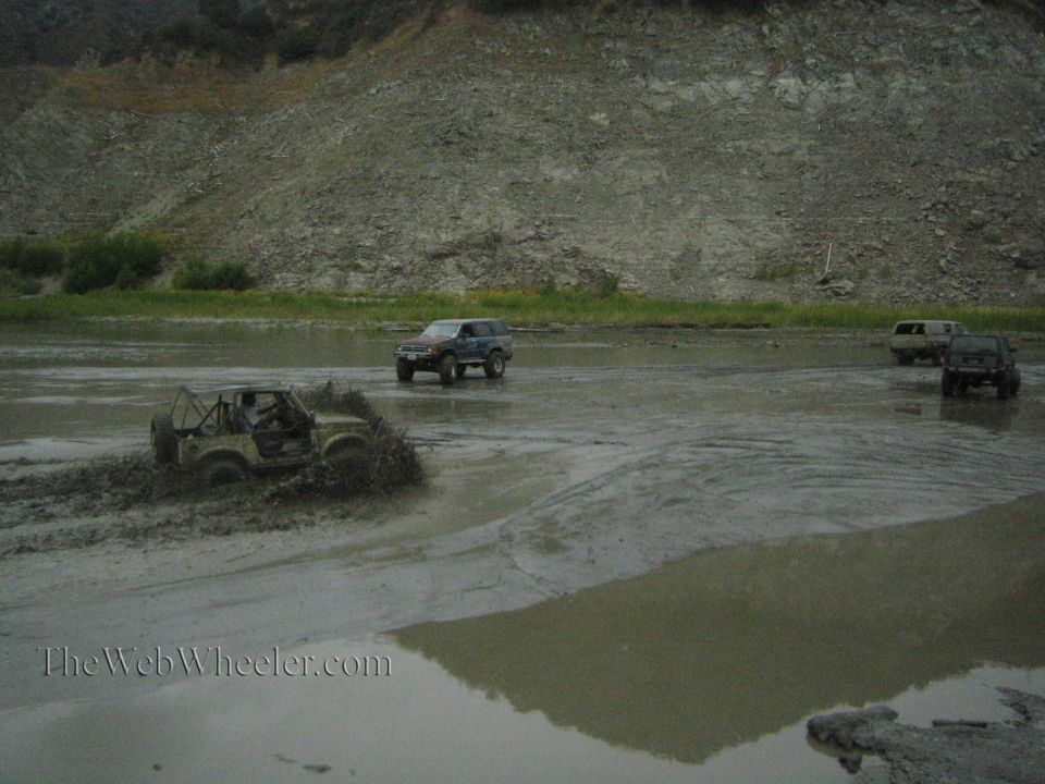 Off-road vehicles navigating a muddy terrain with a rocky hillside in the background