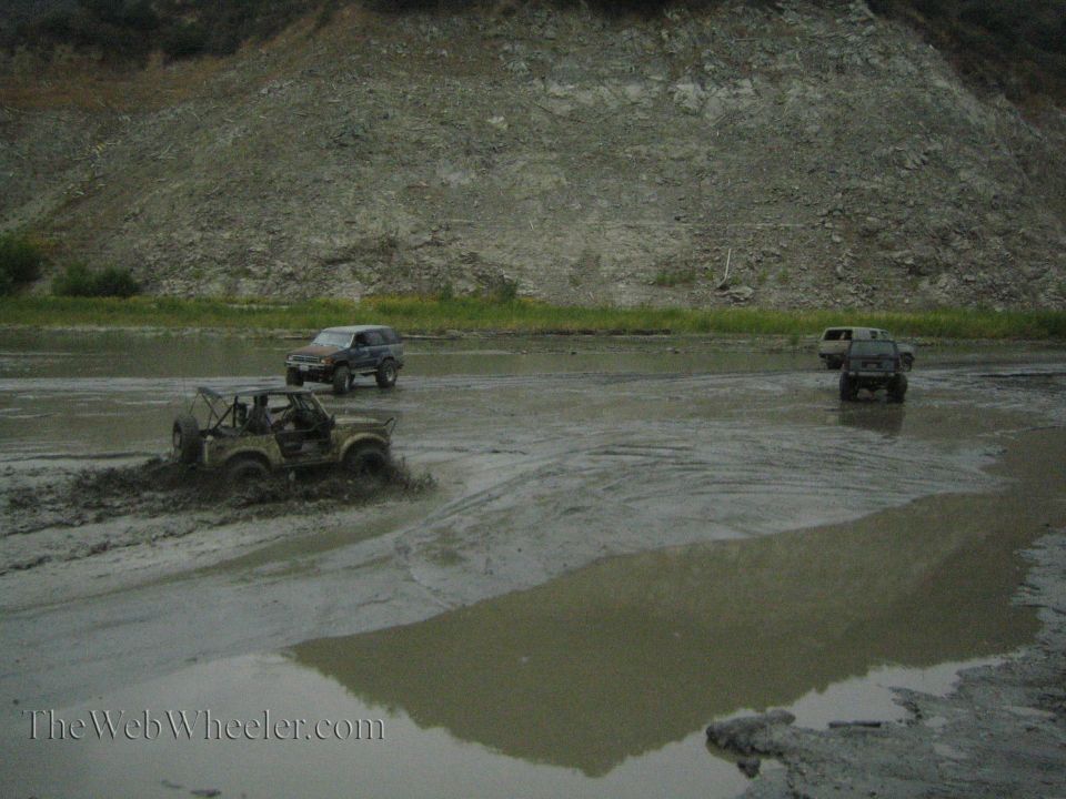 Four-wheel drive vehicles navigating a muddy terrain with one vehicle splashing water