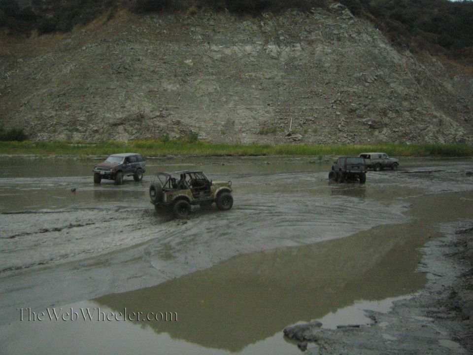 Four-wheel drive vehicles navigating a muddy terrain with a rocky hillside in the background