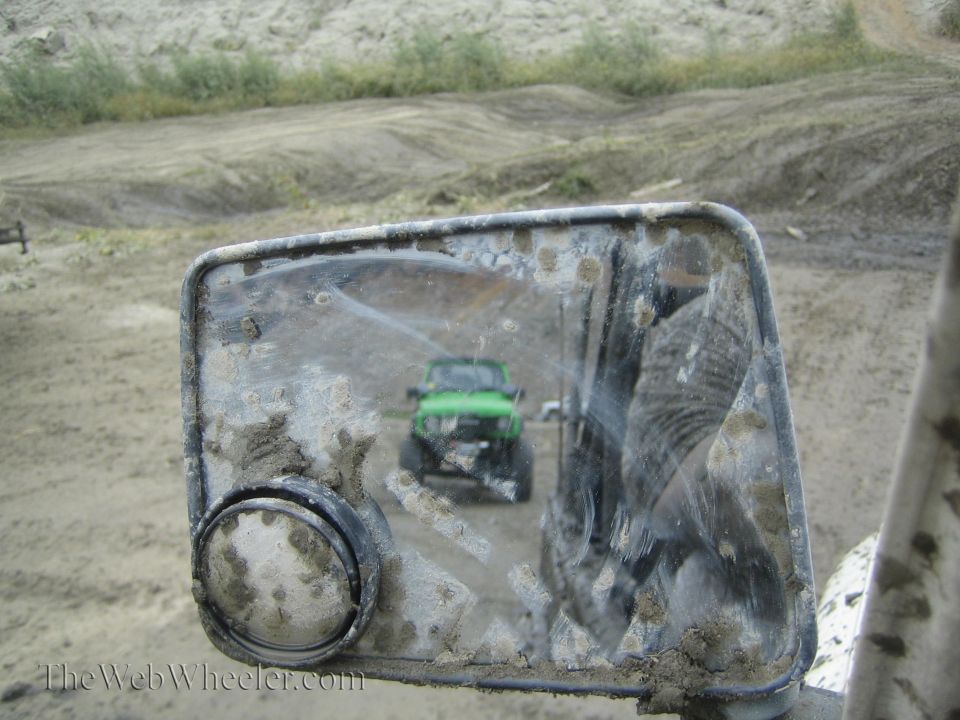 Green Jeep reflected in a dirty side mirror, front view