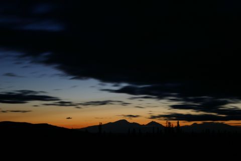 2003 Jeep TJ - A dramatic sunset paints the sky with hues of orange and blue over silhouetted mountains and dark clouds.