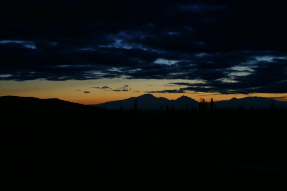 Mountain range silhouetted against a dark sky with orange and blue clouds at dusk
