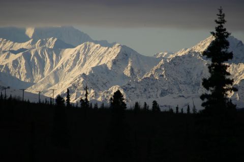 2003 Jeep TJ - A dramatic landscape features snow-covered peaks illuminated by the setting sun, contrasted by a dark, silhouetted forest.