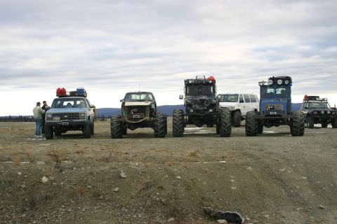 2003 Jeep TJ - Several custom off-road vehicles are lined up on a gravelly surface with a few people nearby.