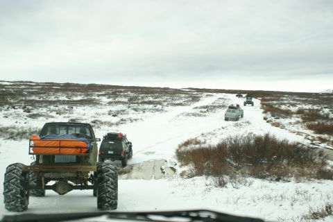 2003 Jeep TJ - A convoy of off-road vehicles navigates a snow-covered trail under an overcast sky.