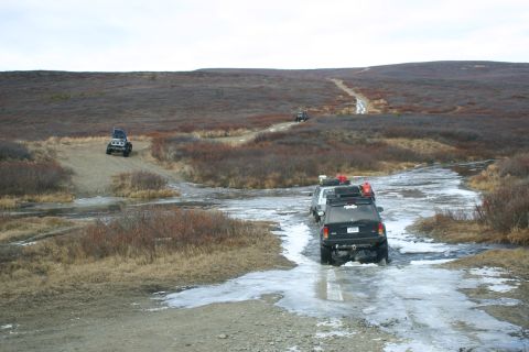 2003 Jeep TJ - Several SUVs navigate a partially frozen dirt road through a barren, brush-filled landscape.