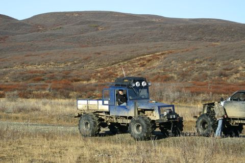 2003 Jeep TJ - Two custom off-road vehicles are parked on a dirt road with hills in the background.