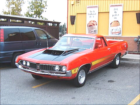1967 Ford Ranchero - A red 1970 Ford Ranchero is parked in front of a building with yellow siding and two large signs.