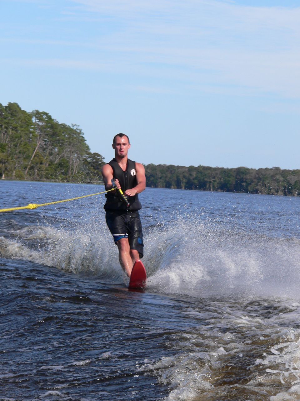 Water skier on a red slalom ski crossing a boat wake on a lake