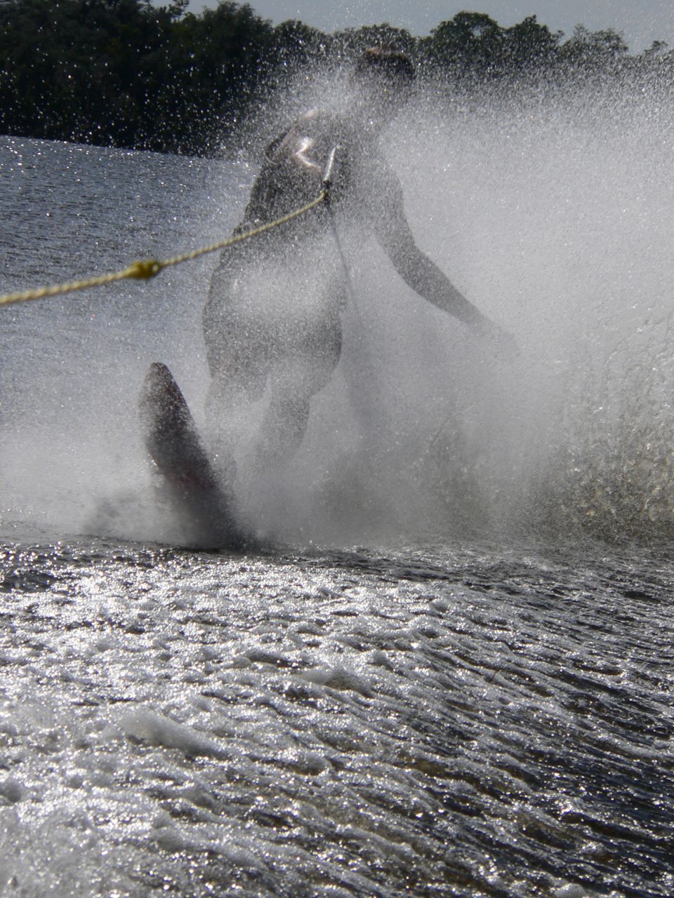 Slalom water-skier throwing a large wall of spray while cutting behind a tow rope