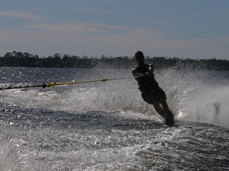 Silhouetted slalom water skier throwing spray while holding a yellow tow rope on a lake
