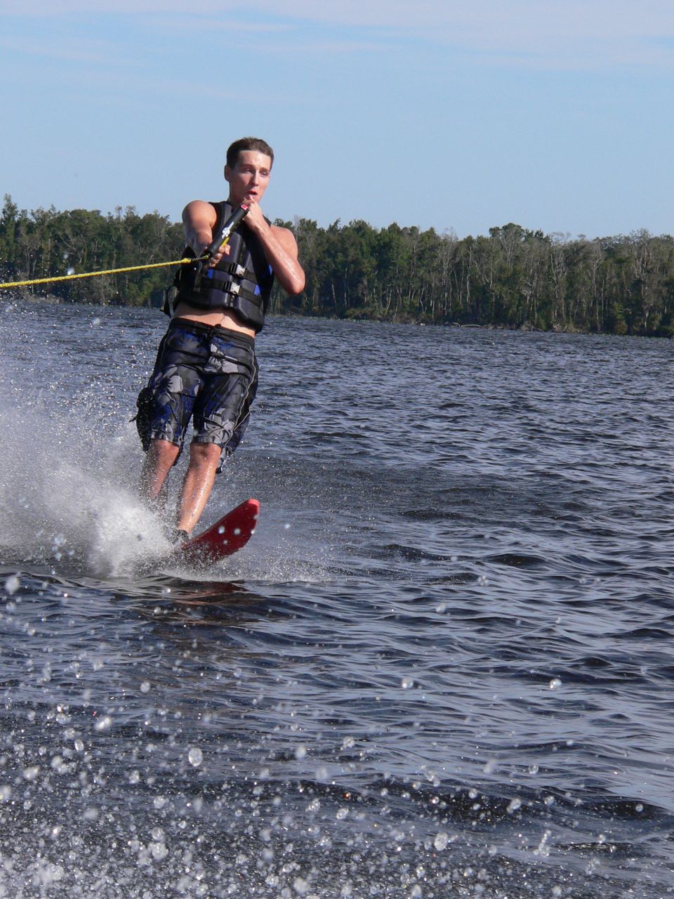 Man slalom water-skiing on a single red ski across a calm lake