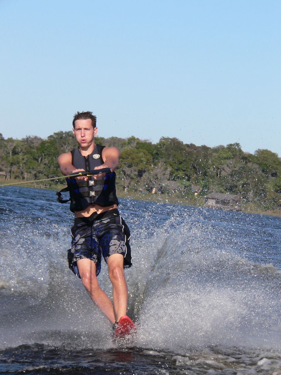 Water skier in black life vest riding a red ski behind a boat on a lake