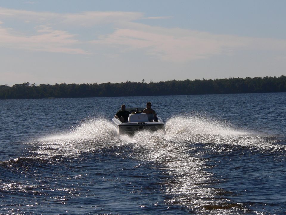 White powerboat with two riders speeding away, throwing a wide spray wake on a lake.