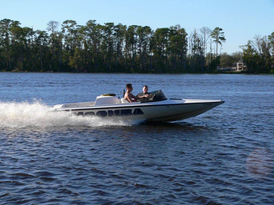 White Moomba speedboat with two people racing across a lake, spraying water.