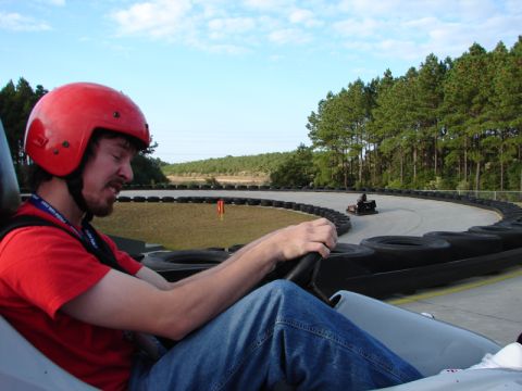 1994 Ford Probe - A driver in a red helmet steers a go-kart around a track, with another go-kart visible in the distance.