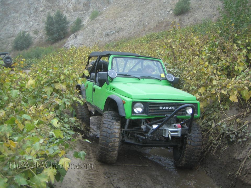 Green 1987 Suzuki Samurai on a muddy trail with off-road tires and a winch