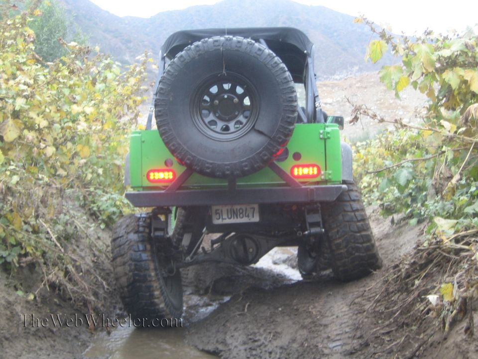 Green off-road vehicle with spare tire on back, driving through mud. License plate reads 5LUN847