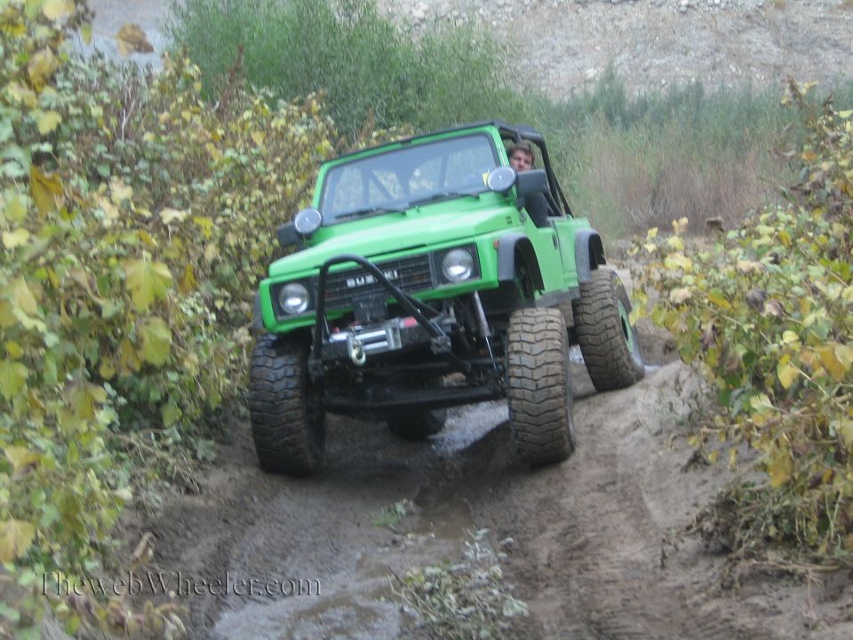 Green 1987 Suzuki Samurai with winch driving on a muddy trail