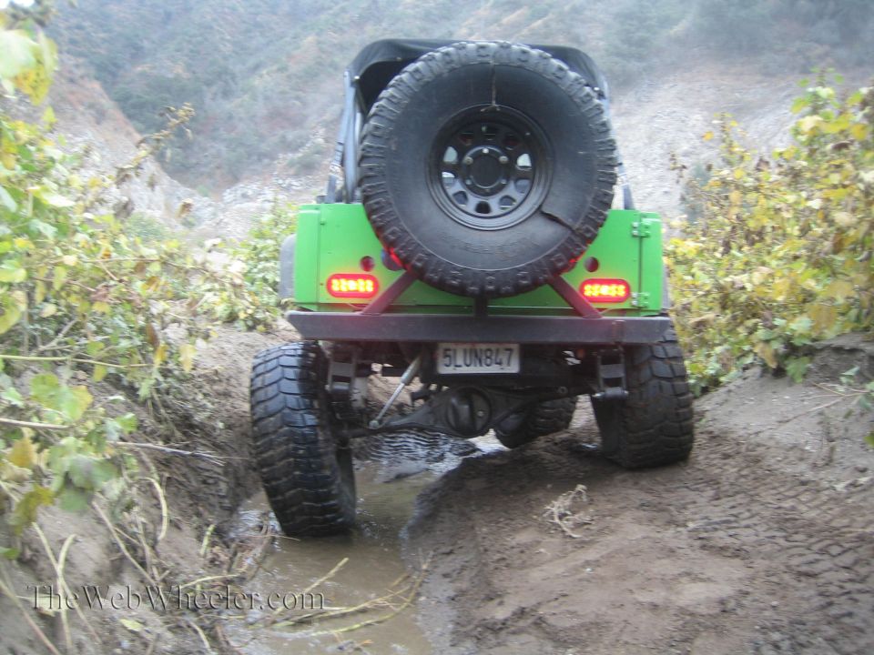 Green off-road vehicle with spare tire on back, driving through mud and water. License plate reads 5LUN847