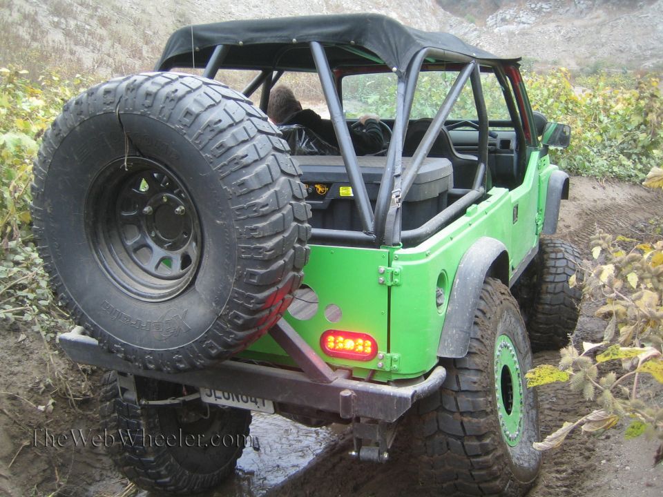 Green 1987 Suzuki Samurai with a spare tire on the back, off-roading on a dirt path