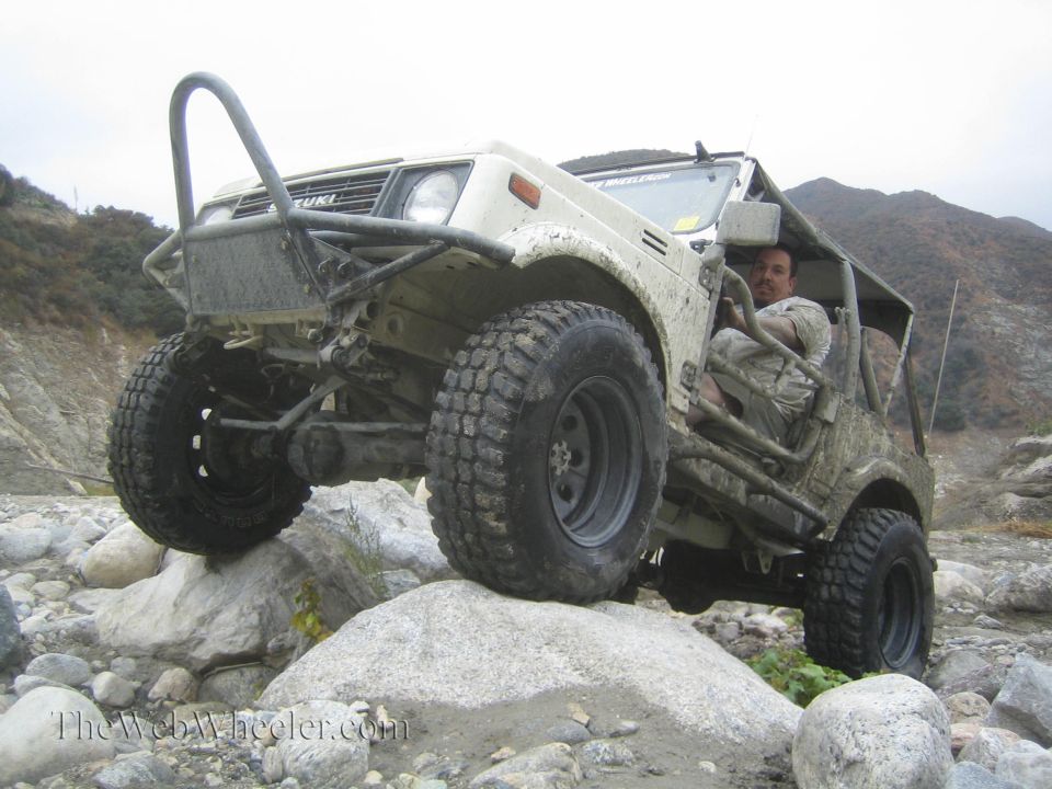 Driver in a 1987 Suzuki Samurai navigating rocks on a trail